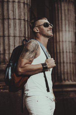 Masculine mature man with backpack standing on a city street. Sightseeing tours, travelling. Active...