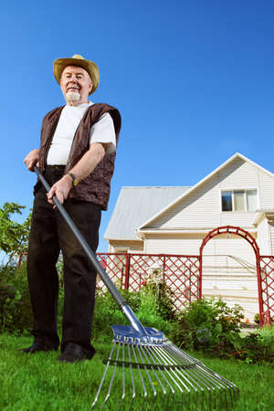 Raking in the garden. Happy senior man gardening in retirement.の写真素材