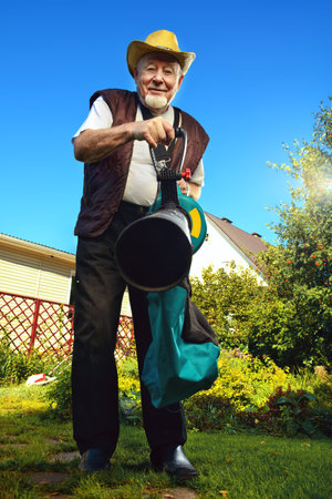 Autumn in a garden. Senior man removes fallen leaves in his garden using leaf blower.