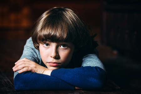 Portrait of a calm and sad boy lying on a floor at home.の写真素材