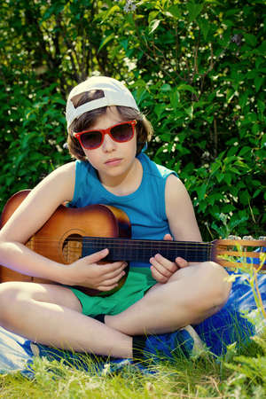 Happy ten year old boy playing guitar and singing a song in the park. Sunny summer holidays.の写真素材