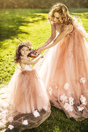 Classical music. Beautiful fairy girl teaches to play the violin a little girl. Musical fairy tales.の写真素材
