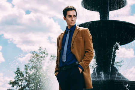 Happy young man in elegant clothes walking in a city park. Outdoor fashion. Business style.の写真素材