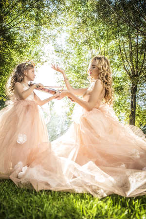 Classical music. Beautiful fairy girl teaches to play the violin a little girl. Musical fairy tales.の写真素材