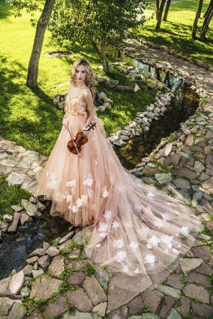 Beautiful fairy girl with the violin in a sunny summer park. Musical concept. Classical music, violin.の写真素材