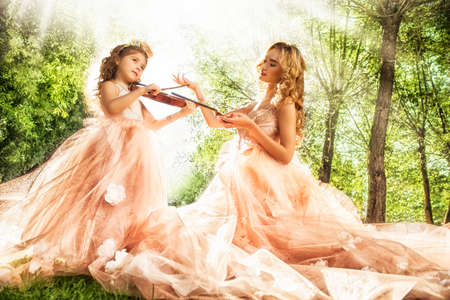 Classical music. Beautiful fairy girl teaches to play the violin a little girl. Musical fairy tales.の写真素材