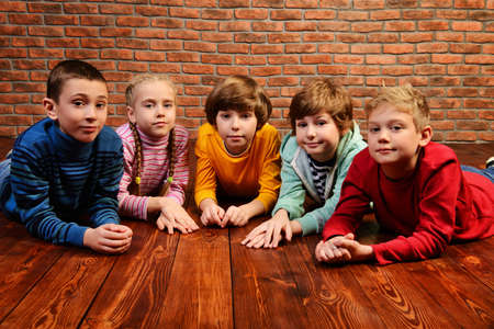 Group of happy children lying on a floor over brick wall background. Kid's fashion. Education.の写真素材