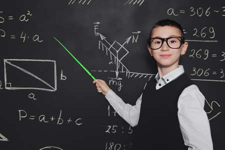 Funny smart boy in formal suit and glasses over school blackboard. Educational concept.の写真素材
