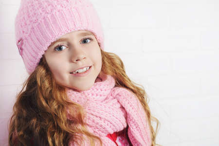 Winter clothes concept. Pretty smiling girl with long curly hair wearing pink knitted hat and scarf and smiling at camera.の写真素材
