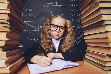 Portrait of a smart schoolgirl in glasses posing with books over school blackboard. Educational concept.の写真素材