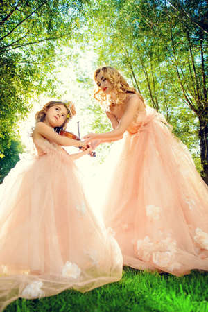 Classical music. Beautiful fairy girl teaches to play the violin a little girl. Musical fairy tales.の写真素材