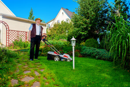 Happy retired senior man mows a lawn in his garden with a lawnmower.
