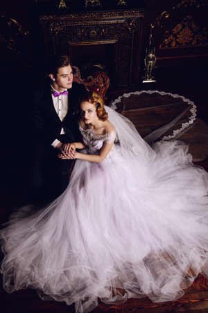 Beautiful bride and groom sitting in tender embrace at a luxurious apartments. Wedding fashion.の写真素材