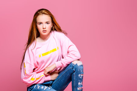 Teen style. Beautiful young model with long hair posing at studio in jeans and pink sweatshirt. Beauty, fashion.の写真素材