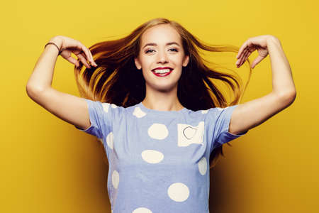 Joyful young woman with beautiful smile posing over yellow background.の写真素材