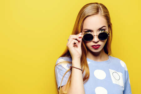 Serious young woman is looking over the sunglasses on a yellow background.の写真素材