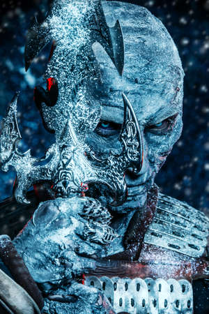 Halloween. Close-up portrait of a frightful snow covered zombie warrior in the armor of a medieval knight holding a sword.の写真素材