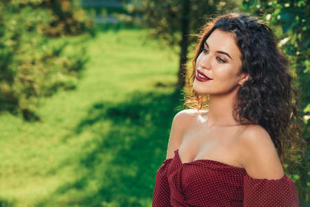 Charming woman dressed in elegant burgundy dress in a summer park. Beauty, fashion concept.の写真素材