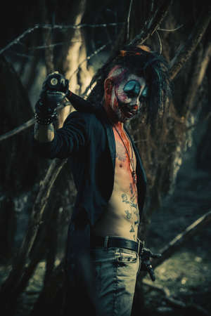 Scary punk clown man smeared with blood in a night forest. Halloween. Horror, thriller film.の写真素材