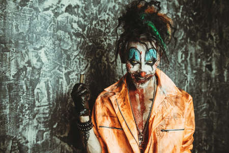 Halloween. Portrait of a disgusting clown man stained in blood over dark background. Male zombie clown. Horror, thriller film.の写真素材