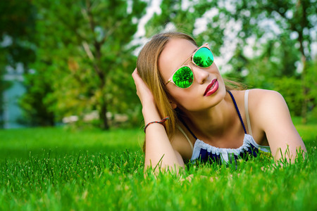 Carefree summer day. Pretty young woman having a rest on a green lawn in a summer park. Beauty, fashion.の写真素材