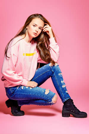 Teen style. Beautiful young model with long hair posing at studio in jeans and pink sweatshirt. Beauty, fashion.の写真素材