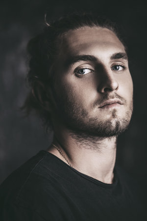 Portrait of a modern young man with long hair. Studio portrait over grunge background. Urban style.