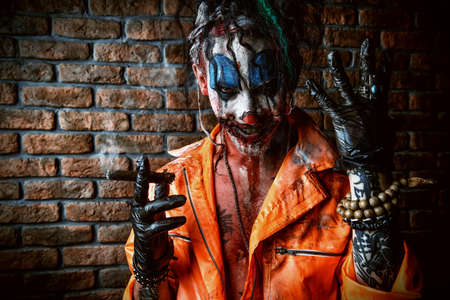 Halloween. Portrait of a bloodthirsty clown man over dark brick wall. Male zombie clown. Horror, thriller film.の写真素材