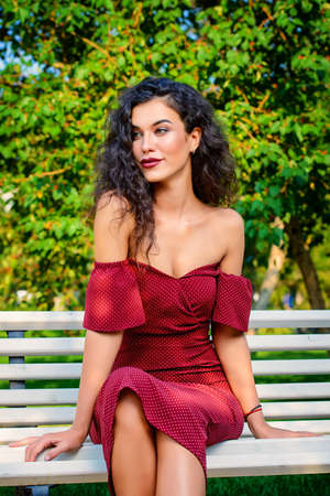 Charming woman dressed in elegant burgundy dress in a summer park. Beauty, fashion concept.の写真素材
