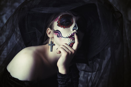 Portrait of a beautiful and scary Calavera Catrina in black dress and black hat with a veil over...