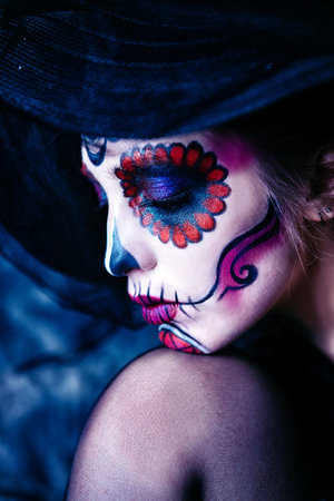 Portrait of a beautiful and scary Calavera Catrina in black dress and black hat with a veil over...