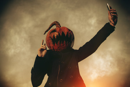 Modern Jack-lantern with a pumpkin on his head is making selfie on a smartphone. Halloween concept.の写真素材