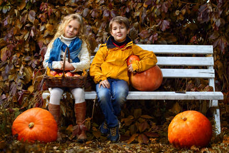 Happy romantic boy and girl sitting on a bench in a beautiful autumn park. Children's fashion. Autumn mood, halloween.の写真素材