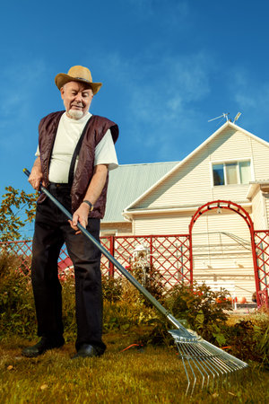 Raking in the garden. Happy senior man gardening in retirement.