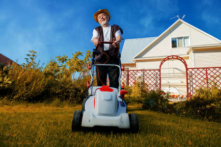 Happy retired senior man mows a lawn in his garden with a lawnmower.の写真素材