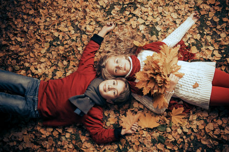 Two cheerful kids lying on a yellow leaves in a beautiful autumn park. Children's fashion. Autumn...