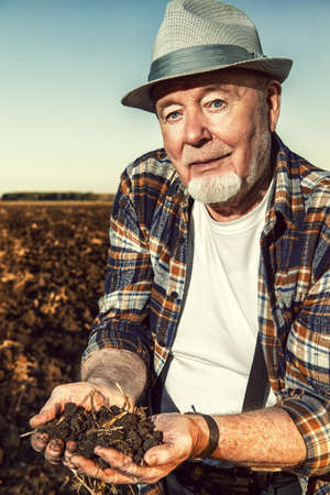An elderly farmer holds a handful of fertile black soil in his hands and smiling. Agriculture, crop concept.の写真素材