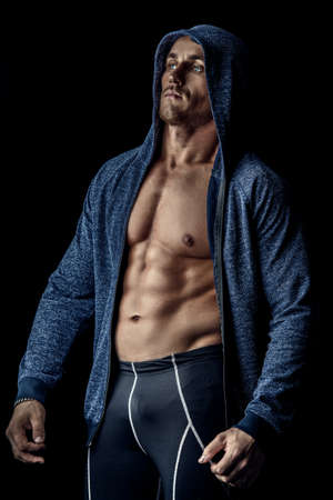 Handsome athletic man in hoodie posing over black background. Sports and bodybuilding concept. Healthy lifestyle.の写真素材