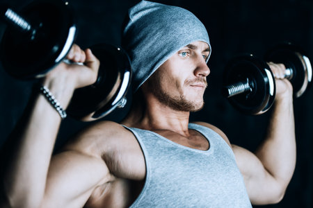 Muscular sportsman bodybuilder doing exercises with dumbbells. Health and sports concept.