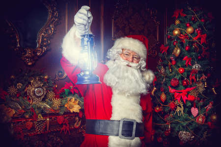 Christmas concept. Portrait of a fairytale Santa Claus standing with lantern in a beautiful Christmas room. Time of miracles.の写真素材