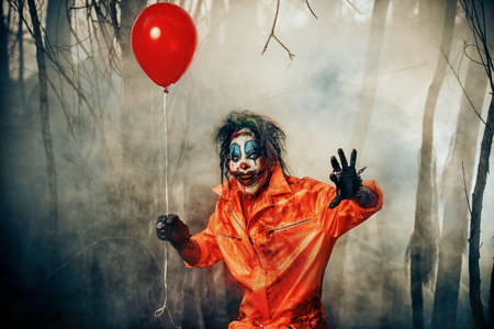 Scary man clown stained in blood in a night forest with a balloon. Male zombie clown. Halloween. Horror.の写真素材