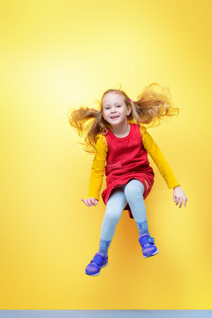 Happy five year old girl in bright summer clothes jumping for joy over yellow background. Happy...