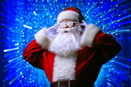 DJ Santa Claus in snowy glasses and headphones. Christmas songs and music. Disco lights in the background.の写真素材