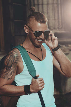 Modern lifestyle. Masculine mature man with backpack standing on a city street and talking on his smartphone. Sightseeing tours, travelling.の写真素材