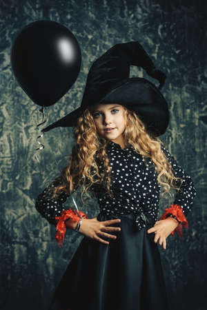 Beautiful child girl in a costume of a witch over grunge background. Halloween party.の写真素材