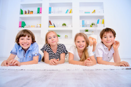 Four funny children lie on the floor at home and laugh. Child concept.の写真素材