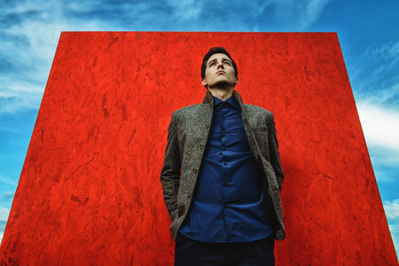 Vogue shot. Handsome fashionable man model posing outdoor over red background and a sky.の写真素材