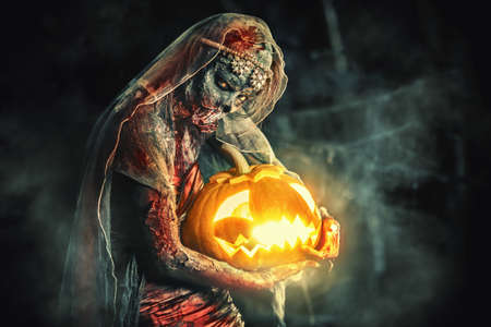 Halloween. Scary zombie bride on a night cemetery holds a pumpkin lantern.の写真素材