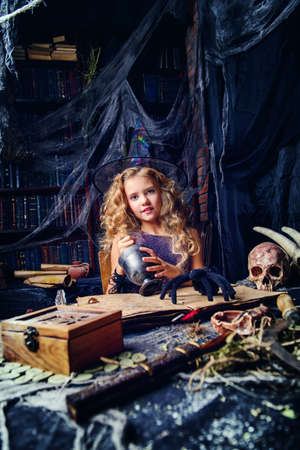 Beautiful charming little witch conjures in her lair. Halloween.の写真素材
