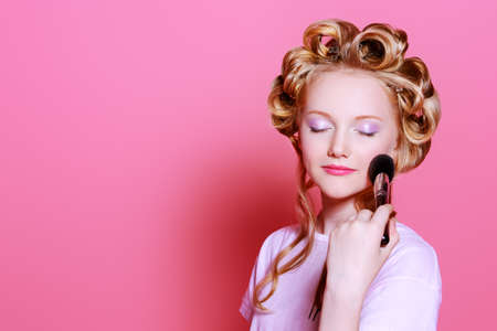 Portrait of a pretty girl teenager with curlers in her blonde hair and brushes. Teen style, fashionable teen girl. Cosmetics and make-up.の写真素材